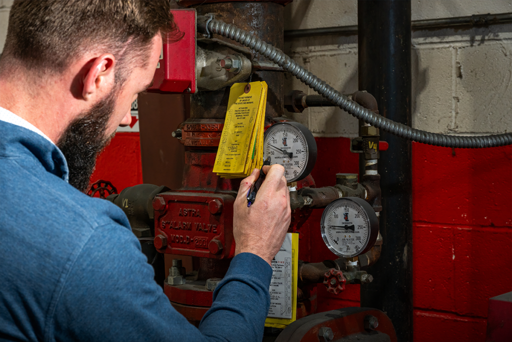 Technician filling out a yellow inspection tag on a fire sprinkler riser after a failed fire inspection