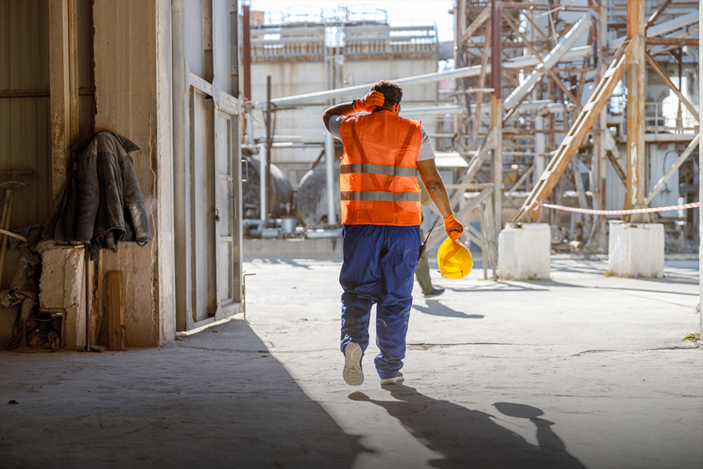 Fire sprinkler fitter walking through an industrial jobsite carrying a hard hat