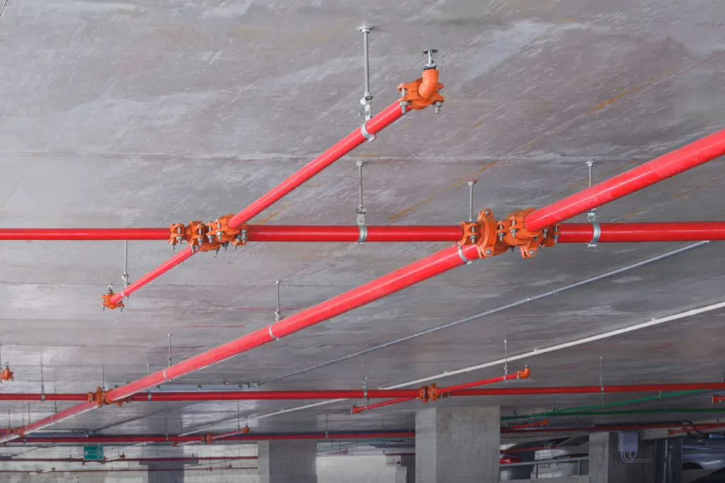 Red fire sprinkler pipe and heads mounted on a concrete ceiling in a parking structure