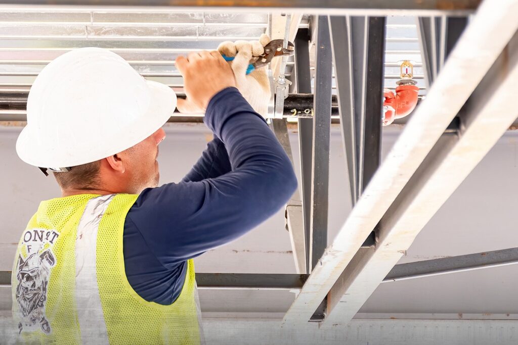 Sprinkler fitter in a hard hat installing overhead pipe on a commercial jobsite