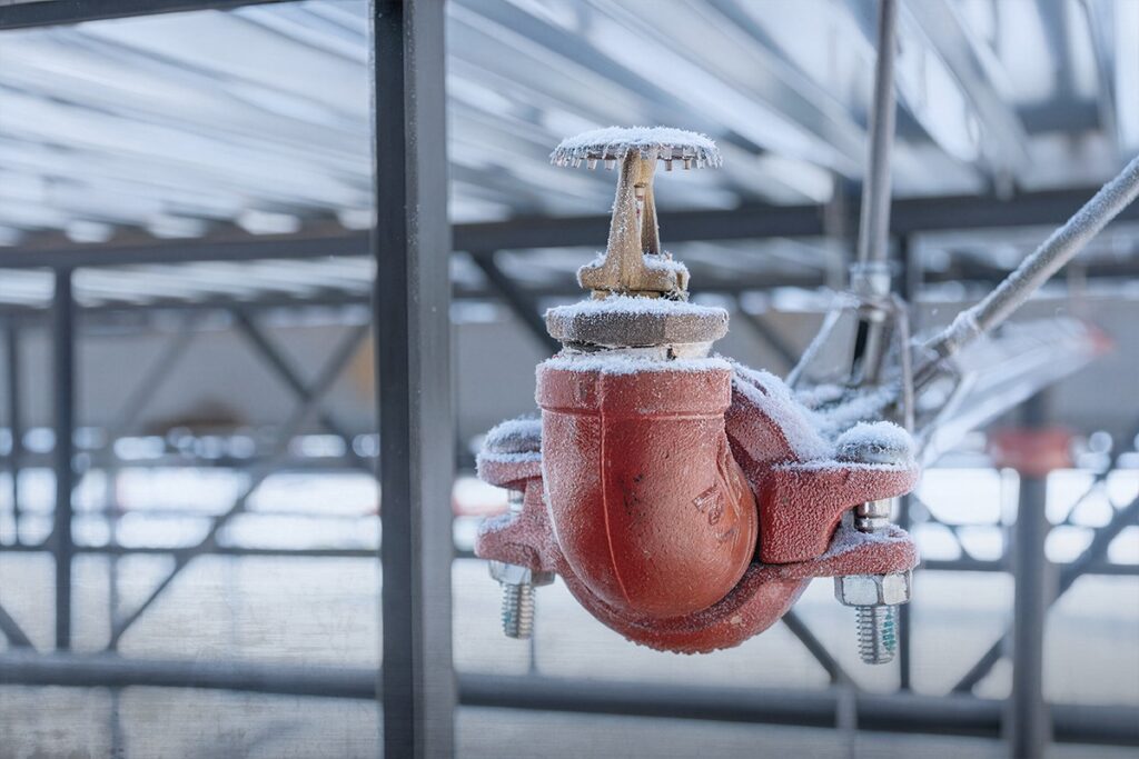 Frost covered fire sprinkler valve on exposed steel piping in winter
